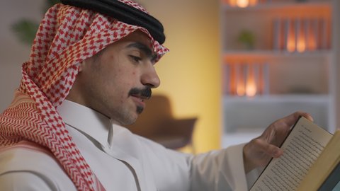 الاستمتاع بالهدوء والراحة داخل المنزل، قضاء الوقت بالمطالعة والثقافة، ممارسة الهوايات المفضلة،رجل عربي خليجي سعودي يرتدي الزى التقليدي مع الشماغ يجلس على الأريكة في غرفة المعيشة ويقوم بقراءة كتاب ، الاستمتاع بقراءة الروايات والقصص ، تعزيز مفهوم الثقافة والمعرفة ، تنمية المهارات الفكرية