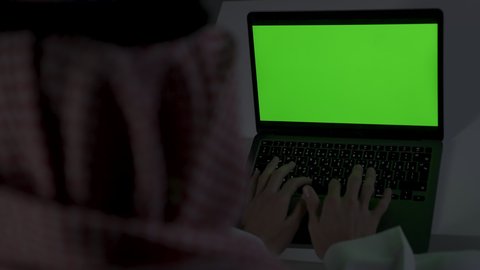 Green screen chroma key display, Saudi jobs and professions, remote business management, completing required tasks via laptop, integrating advanced technologies into daily life, development and modern technology, a Saudi Arabian Gulf man wearing traditional clothing with a keffiyeh sitting on a couch in a dark room using a laptop, using a laptop.