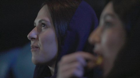تناول الفوشار اثناء متابعة أفلام التشويق والاثارة، تصوير مقرب من الجانب لصديقتان عربيان خليجيتان سعوديتان يقومان بقضاء وقت ممتع في السينما، الاستمتاع بالأنشطة الترفيهيه في العطلة، ايماءات الاندماج و التركيز