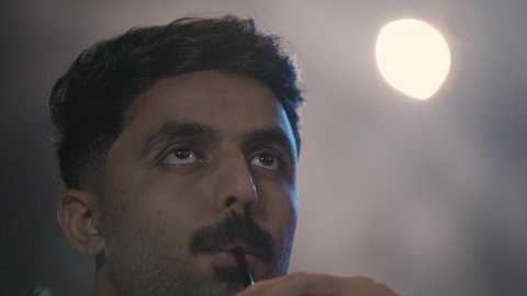 The feeling of refreshment while having drinks, a close-up shot of a Saudi Arabian Gulf man wearing a white thobe sitting inside the cinema watching a movie, gestures of engagement and focus.