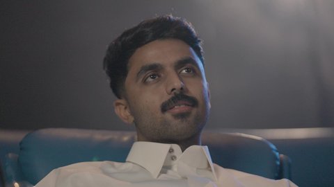 ممارسة أنشطة ترفيهية وقضاء لحظات ممتعة في الخارج، تصوير مقرب لرجل عربي خليجيسعودي  يرتدي الثوب الابيض يجلس داخل السينما يقوم بمشاهدة الفيلم، ايماءات الاندماج و التركيز