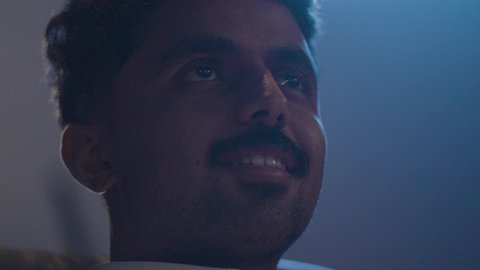 Enjoying recreational activities outside the home, a close-up shot of a Saudi Arabian Gulf man wearing a white thobe sitting inside the cinema watching a movie, gestures of engagement and focus.
