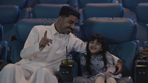 نشاط عائلي ترفيهي، رجل خليجي يرتدي الثوب الابيض يجلس برفقه ابنته داخل القاعه ، الاستمتاع بتناول المشروبات ، ايماءات السعادة و السرور ، قضاء عطله نهايه الاسبوع