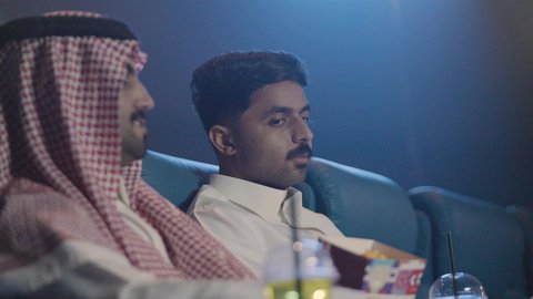 مشاركة تناول الفشار ، شابان عربيان خليجيان سعوديان يرتديان الزي التقليدي يقومان بمشاهده فيلم سينما ،  الترفيه عن النفس، قضاء أوقات ممتعة ومسلية ، عطلة نهاية الإسبوع