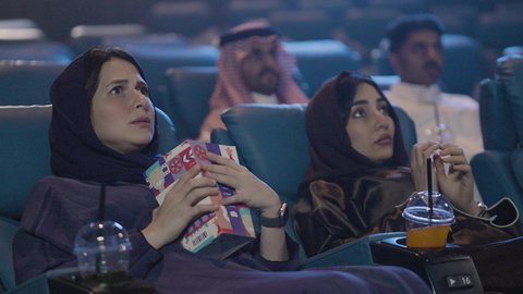 مشاهدة الأفلام السينمائية، عطلة نهاية الأسبوع ، قضاء أوقات ممتعة ، ايماءات الاندماج و التركيز و التفاعل ، تناول الفشار أثناء مشاهدة العروض، تصوير مقرب لصديقتان عربيتان خليجيتان يرتديان الحجاب يجلسان في صالة السينما، مشاركة الفشار، تناول المشروبات المفضلة