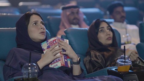 قضاء أوقات ممتعة , عطلة نهاية الأسبوع ، مشاهدة الأفلام السينمائية ، ايماءات الاندماج والخوف، تناول الفشار أثناء مشاهدة العروض، تصوير مقرب لصديقتان عربيتان خليجيتان يرتديان الحجاب يجلسان في صالة السينما، مشاركة الفشار، تناول المشروبات المفضلة
