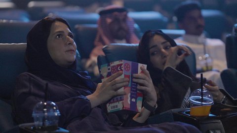 ممارسة أنشطة ممتعة، الاستمتاع بمشاهدة الأفلام ، ايماءات الاندماج و الدهشه،تناول الفشار أثناء مشاهدة العروض، تصوير مقرب لصديقتان عربيتان خليجيتان يرتديان الحجاب يجلسان في صالة السينما، مشاركة الفشار، أنشطه ترفيهيه، تناول المشروبات المفضلة