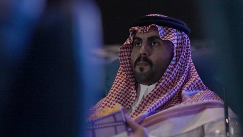 الاستمتاع بأكل دلو الفشار، تعابير وجه و يدين تدل على الحماس و الاستمتاع ، نشاط ترفيهي ، دور العرض، متابعة الأفلام والمسرحيات على شاشة السينما، تصوير مقرب لرجل عربي خليجي سعودي يرتدي الزي التقليدي سجلس  في صالة السينما