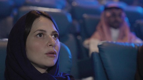 متابعة الأفلام والمسرحيات على شاشة السينما، ايماءات الاندماج و الدهشه و التركيز، تصوير مقرب لامراة عربيه خليجيه سعودية تجلس في صالة السينما، أنشطه ترفيهيه