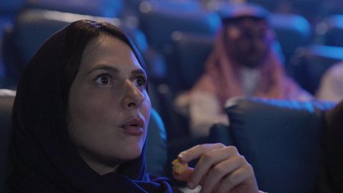 قضاء وقت ممتع في السينما لمشاهدة العروض، ايماءات الاندماج و الدهشه، تناول الفشار أثناء مشاهدة العروض، تصوير مقرب لامراة عربيه خليجيه سعودية تجلس في صالة السينما، أنشطه ترفيهيه