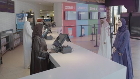 سينما ومسرح، تصوير مقرب لإمرأه عربيه سعوديه خليجيه تبيع المأكولات والمشروبات في ردهة الإستقبال داخل السينما تقوم بالنقر على الشاشة، زبونه خليجيه ترتدي العباءة و الحجاب تقوم بطلب سناكس, الإستعداد للدخول الى صالة العرض، مشاهدة الأفلام والعروض المسرحية، أنشطه ترفيهيه