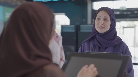 أنشطه ترفيهيه، ايماءات السعادة و السرور، الإستعداد للدخول الى صالة العرض، تصوير مقرب من الخلف لإمرأه عربيه سعوديه خليجيه تبيع المأكولات والمشروبات في ردهة الإستقبال داخل السينما تقوم بالنقر على الشاشة، سينما ومسرح، زبونه تقوم بشراء سناكس