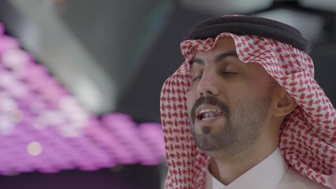 Preparing to enter the screening room, a close-up shot of a Saudi Arabian Gulf man wearing traditional attire and a ghutrah buying snacks, selling food and drinks in the reception area inside the cinema.