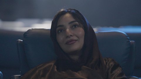 تعابير تدل على السعادة والإندماج, أنشطة ترفيهية، قضاء أوقات ممتعة، مشاهدة الأفلام والعروض المسرحية في السينما، تصوير مقرب لامراة عربيه خليجيه سعودية ترتدي الحجاب تجلس في صالة السينما، سينما ومسرح، دور العرض