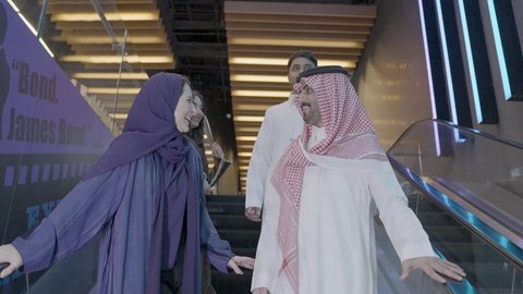 The pleasure of shopping and buying in Saudi malls, strolling and going up the escalators, a group of Arab Gulf friends from Saudi Arabia wearing traditional attire using the escalator, enjoying spending quality time with family, buying necessities and gifts.