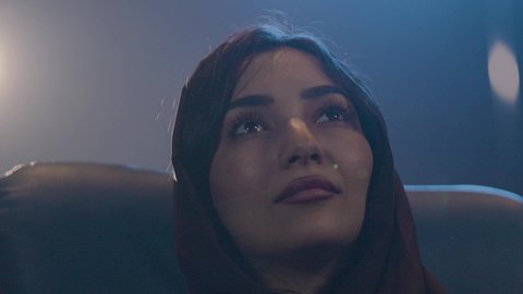 Recreational activities, spending enjoyable times, watching movies and theatrical performances in the cinema, a close-up shot of an Arab Gulf Saudi woman wearing a hijab sitting in the cinema hall, expressions indicating happiness and engagement, cinema and theater, screening venues.