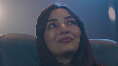 مشاهدة الأفلام والعروض المسرحية في السينما، تصوير مقرب لامراة عربيه خليجيه سعودية ترتدي الحجاب تجلس في صالة السينما، تعابير تدل على السعادة والإندماج، أنشطة ترفيهية، قضاء أوقات ممتعة، سينما ومسرح، دور العرض