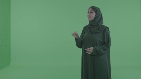 التحكم بالهولوجرامات عبر لمس الشاشة وحركات اليد، امراة عربيه خليجيه سعودية ترتدي الحجاب و العباءة تقوم بالرسم والتخطيط في الهواء، محاكاة العالم الخيالي، خلفية خضراء ، كروما