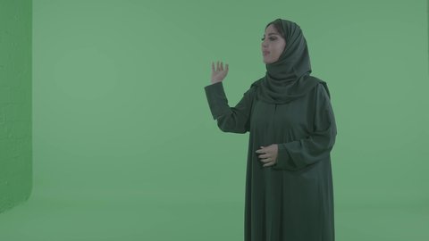 استخدام اللمس للتحكم بالعناصر الهولوجرامية، امراة عربيه خليجيه سعودية ترتدي الحجاب و العباءة  تقوم بالرسم والتخطيط في الهواء، محاكاة العالم الخيالي، خلفية خضراء ، كروما
