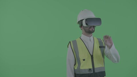 التحكم بالنماذج الهندسية عبر الواقع الافتراضي، نمو المجال الهندسي التكنولوجي، بورترية لمهندس عربي خليجي سعودي يرتدي سترة العمل و الخوذة ونظارة الفي آر يتفاعل مع مجسم لمخطط بناء هولوجرامي، خلفية خضراء ، كروما