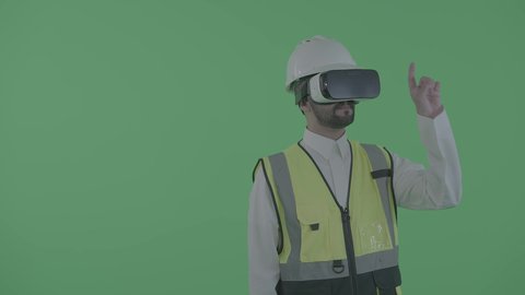 التفاعل مع التصاميم الهندسية ثلاثية الأبعاد، نمو المجال الهندسي التكنولوجي، العمل بالقطاع الهندسي عبر تقنية الواقع الافتراضي، بورترية لمهندس عربي خليجي سعودي يرتدي سترة العمل و الخوذة ونظارة الفي آر يتفاعل مع مجسم لمخطط بناء هولوجرامي، خلفية خضراء ، كروما