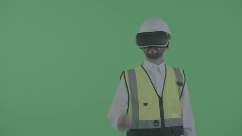 التعامل مع النماذج الهندسية الرقمية، نمو المجال الهندسي التكنولوجي، العمل بالقطاع الهندسي عبر تقنية الواقع الافتراضي، بورترية لمهندس عربي خليجي سعودي يرتدي سترة العمل و الخوذة ونظارة الفي آر يتفاعل مع مجسم لمخطط بناء هولوجرامي، خلفية خضراء ، كروما
