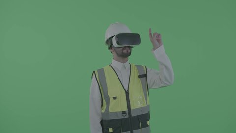 التفاعل مع الهندسة الافتراضية، العمل بالقطاع الهندسي عبر تقنية الواقع الافتراضي، بورترية لمهندس عربي خليجي سعودي يرتدي سترة العمل و الخوذة ونظارة الفي آر يتفاعل مع مجسم لمخطط بناء هولوجرامي، نمو المجال الهندسي التكنولوجي، خلفية خضراء ، كروما