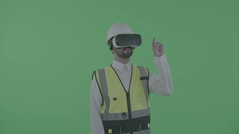 العمل بالقطاع الهندسي عبر تقنية الواقع الافتراضي، التفاعل مع الهندسة الافتراضية، بورترية لمهندس عربي خليجي سعودي يرتدي سترة العمل و الخوذة ونظارة الفي آر يتفاعل مع مجسم لمخطط بناء هولوجرامي، نمو المجال الهندسي التكنولوجي، خلفية خضراء ، كروما