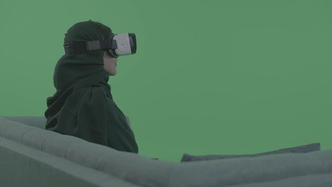 الاندماج والتفاعل مع العالم الافتراضي، الاستمتاع في قضاء الأوقات الترفيهية، استخدام تقنيات حديثة الكترونية وأجهزة تكنولوجية، بورترية لشابة عربية خليجية سعودية محجبة تجلس على الاريكه تضع نظارات الفي آر ثلاثية الابعاد، خلفية خضراء ، كروما