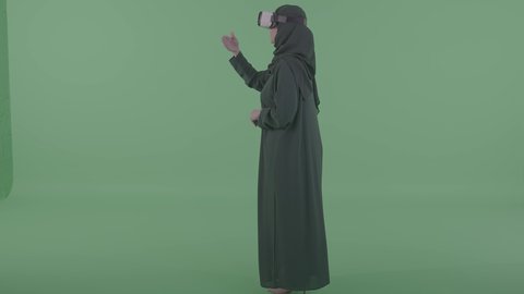 التحكم  بعنصر ما عبر لمس الشاشة، بورترية من الجانب لامراة عربيه خليجيه سعودية محجبه ترتدي العباءة والنظارة نظارات ثلاثية الأبعاد (الفي ار) ، تعابير النقر على شاشة ، محاكاة العالم الخيالي، خلفية خضراء ، كروما