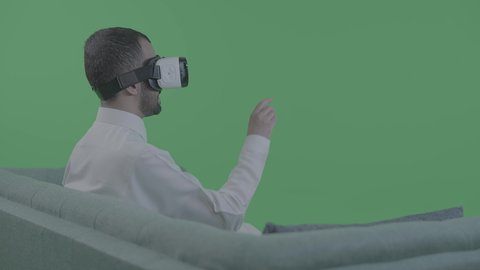 استخدام حاسة اللمس لتحريك عنصر ما، بورترية من الخلف لرجل عربي خليجي سعودي يجلس على الاريكه يرتدي الثوب و الابيض و النظارة نظارات ثلاثية الأبعاد (الفي ار) يقوم بايماءات الترحيب، تعابير النقر على شاشة ، محاكاة العالم الخيالي، خلفية خضراء ، كروما