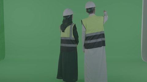 ارتداء سترة وخوذة الامان والحماية، الإشراف والتدقيق على العمل، مهن ووظائف سعودية، بورترية من الخلف لمهندس عربيى خليجي سعودي يقوم بالتعاون ومتابعة الاعمال والمخططات برفقة زميلتة، خلفية خضراء ، كروما