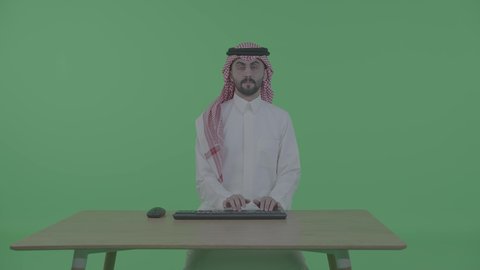مفهوم ادخال البيانات، دمج التكنولوجيا الحديثة بالحياة العملية، مهن ووظائف إدارية مكتبية، صناعة المحتويات النصية، بورترية لرجل عربي خليجي سعودي يرتدي الزي التقليدي و الشماغ يجلس على الطاوله يقوم بالنقر على لوحة المفاتيح ، ايماءات التفكير فى شيء ما، خلفية خضراء ، كروما