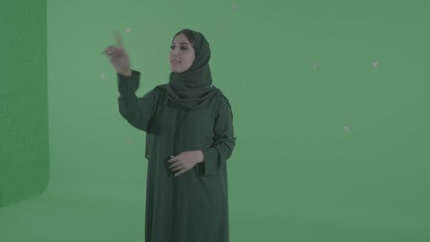 Screen tapping expressions, using the sense of touch to move holographic elements, an Arab Gulf Saudi woman drawing and planning in the air, simulating a fantasy world, green background, chroma.