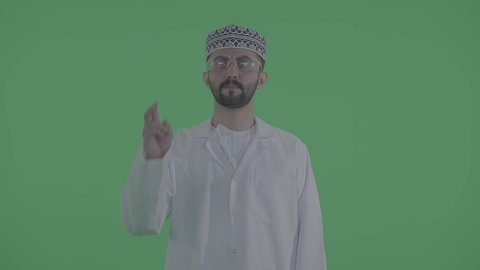 التفاعل مع الشاشة باللمس وتحريك العناصر الافتراضية، تصوير مقرب لرجل عربي خليجي عماني يرتدي الدشداشة و الكمه يقوم بالرسم والتخطيط في الهواء، محاكاة العالم الخيالي، خلفية خضراء ، كروما