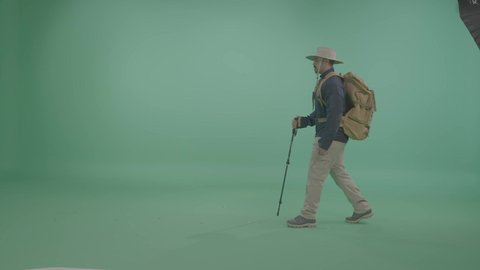 المشي والذهاب الى مكان ما، نشاطات المغامرة والتخييم في الهواء الطلق، بورترية لمستكشف عربي خليجي سعودي يرتدي ملابس جبلية مناسبة للتنقل والسفر يحمل عصا المشي، الاستعداد للمغامرات السياحية، الجسم بالطول الكامل ، خلفية خضراء ، كروما