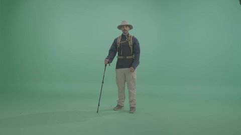Adventure and camping activities in the outdoors, an Arab Gulf Saudi explorer wearing suitable mountain clothing for mobility and travel, carrying a walking stick, ready for tourist adventures, looking at the camera with gestures of happiness and joy, full-body shot, green background, chroma.