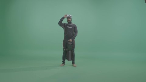 The concept of marine and recreational activities, a portrait of an Arab Gulf Saudi man wearing a diving suit and swimming goggles, preparing for a deep-sea diving adventure, full-body, green background, chroma.