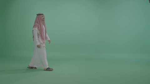 الاهتمام بالمظهر الخارجي، مفهوم الأناقة والرجولة والقوة, ايماءات المشي و الذهاب إلى مكان معين، بورتريه لرجل عربي خليجي سعودي يرتدي الزي التقليدي و الشماغ يتقدم إلى الأمام بخطوات ثابتة، الجسم بالطول الكامل ، خلفية خضراء ، كروما