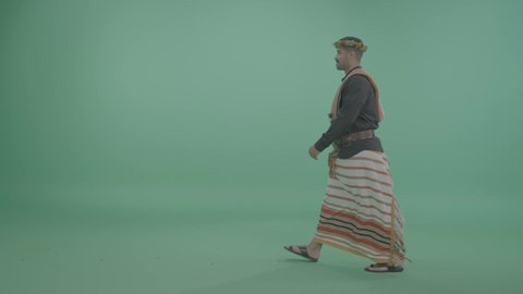 Gestures of walking and going to a specific place, events and recreational activities in Saudi Arabia, a portrait of a Saudi Gulf Arab man wearing the Jizani attire, green background, chroma.