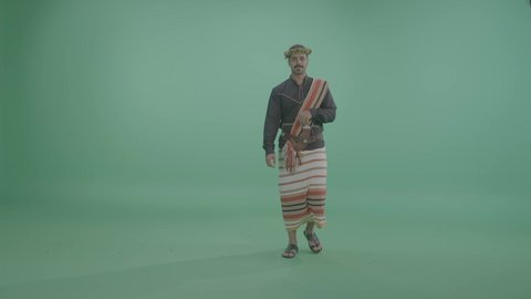 Expressions of welcome and reception, events and recreational activities in Saudi Arabia, a portrait of a young Arab Gulf Saudi man wearing the Jizan outfit greeting and saluting, celebrating Saudi National Day on September 23, green background, chroma.