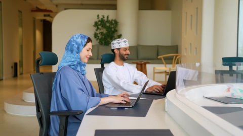 بيئة العمل المريحة في الشركات العمانية، إنجاز المهام المكتبية باستخدام الحاسب المحمول ,رجلان عربيان خليجيان يرتديان الثوب التقليدي يتصافحان في مقر الشركة, العمل في الشركات العمانية الراقية، امراة عربيه خليجيه عمانية محجبه تقوم بالعمل على الابتوب بايماءات الاندماج و التركيز