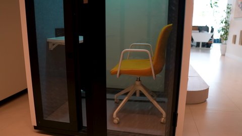 تجهيزات مكتبية حديثة، تصوير مقرب لكرسي مكتبي أصفر داخل غرفة زجاجية حديثة التصميم، ديكورات مكاتب عصرية، مفهوم العزل الصوتي في بيئة العمل ، بيئة مكتبية أنيقة