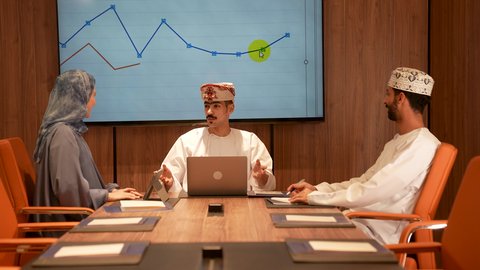 Team discussions and dialogues, the concept of partnership and cooperation, providing a suitable work environment, Arab Omani Gulf employees in a meeting, wearing traditional Omani attire, success and achieving goals, using modern devices and technologies in completing office work.