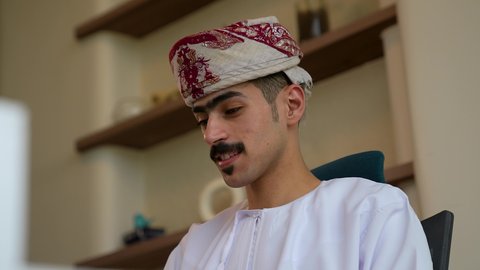 إدارة شؤون الأعمال وتنظيمها ، إنجاز مهام العمل، تصوير مقرب  لرجل عربي خليجي عماني يرتدي الدشداشة و العمامة يجلس داخل الشركة ، ايماءات الاندماج و التركيز