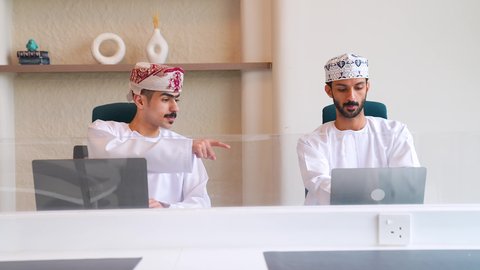 الاشارة الى شي ما، إدارة شؤون الأعمال وتنظيمها، تصويرلرجل عربي خليجي عماني يرتدي الزي التقليدي يقوم بالعمل على الحاسوب داخل المكتب برفقة زميله، العمل لتحقيق الاهداف والاستراتيجيات، مهن ووظائف ادارية مكتبية, استخدام الأجهزة التكنولوجية الحديثة والمتطورة