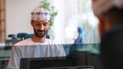 إدارة سير الأعمال عبر الحاسوب المحمول، مفهوم الإشراف على العمل، الاستفادة من التقنيات الحديثة في القطاع المكتبي والإداري،رجل عربي خليجي عماني يرتدي الدشداشه والكمه يجلس خلف طاولة المكتب يقوم باستخدام الحاسب المحمول