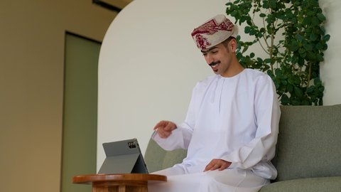 إجراء مكالمة فيديو عبر التابلت، استخدام التقنيات الحديثة في التواصل مع العملاء، رجل عربي عماني يرتدي الدشداشة و العمامة يجلس في مكتبه يجري محادثة عبر الانترنت، ايماءات القبول و الموافقة