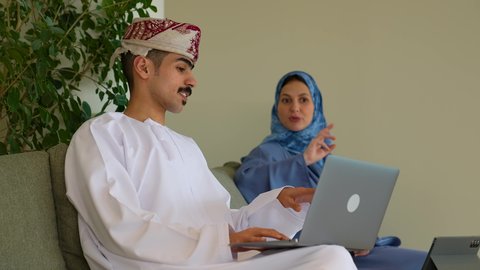 ضمان فهم واضح للاعمال، التركيز والعمل الجاد، مناقشة الخطوات القادمة، تصوير مقرب لامراة عربيه خليجيه عمانية محجبة ترتدي العباءة تجلس برفقة زميلها  تقوم  بإبداء الرأي ومشاركة الأفكار، رجل عربي خليجي عماني يرتدي الدشداشة و العمامة يقوم باستخدام الحاسوب المحمول