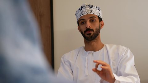 مناقشة الخطوات القادمة، تصوير مقرب لرجل عربي خليجي عماني يرتدي الدشداشة و الكمه يجلس داخل غرف الاجتماعات و يقوم بإبداء الرأي ومشاركة الأفكار، الحوارات والنقاشات ضمن الفريق، ضمان فهم واضح للاعمال، التركيز والعمل الجاد، الاحترافية في الإنجاز